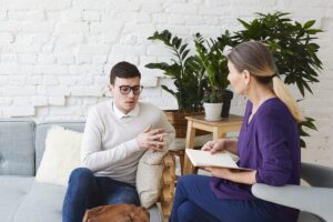 a man sits on a couch and discusses his concerns with his therapist in a bipolar disorder treatment program