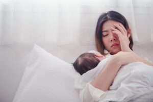 a woman tries to comfort her baby in bed while struggling with symptoms of postpartum depression 
