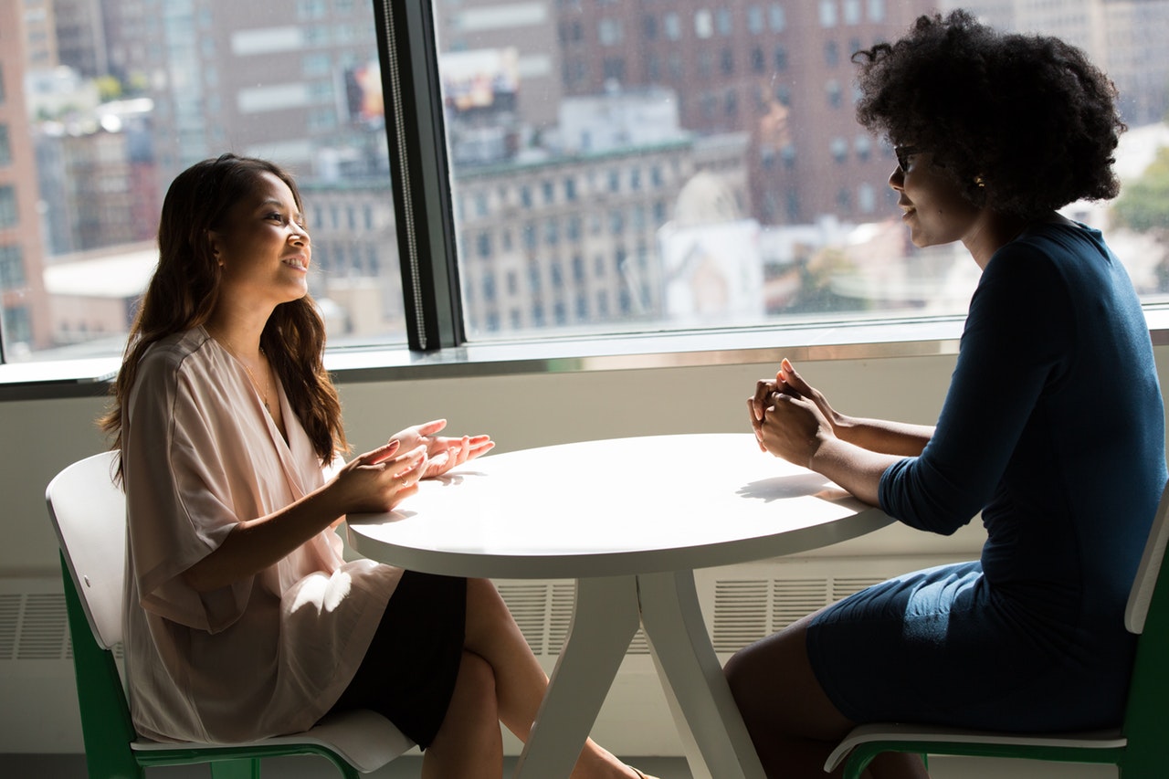 Two women sit across the table from one another talking