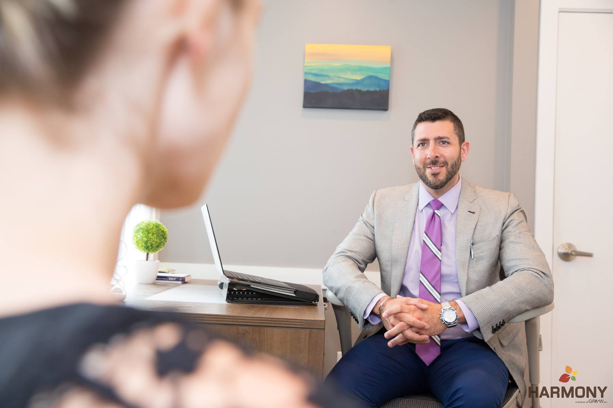 a female patient in the left corner of the screen faces dr. wakin, a man with short brown hair and a beard, who is sitting across from her during a therapy session