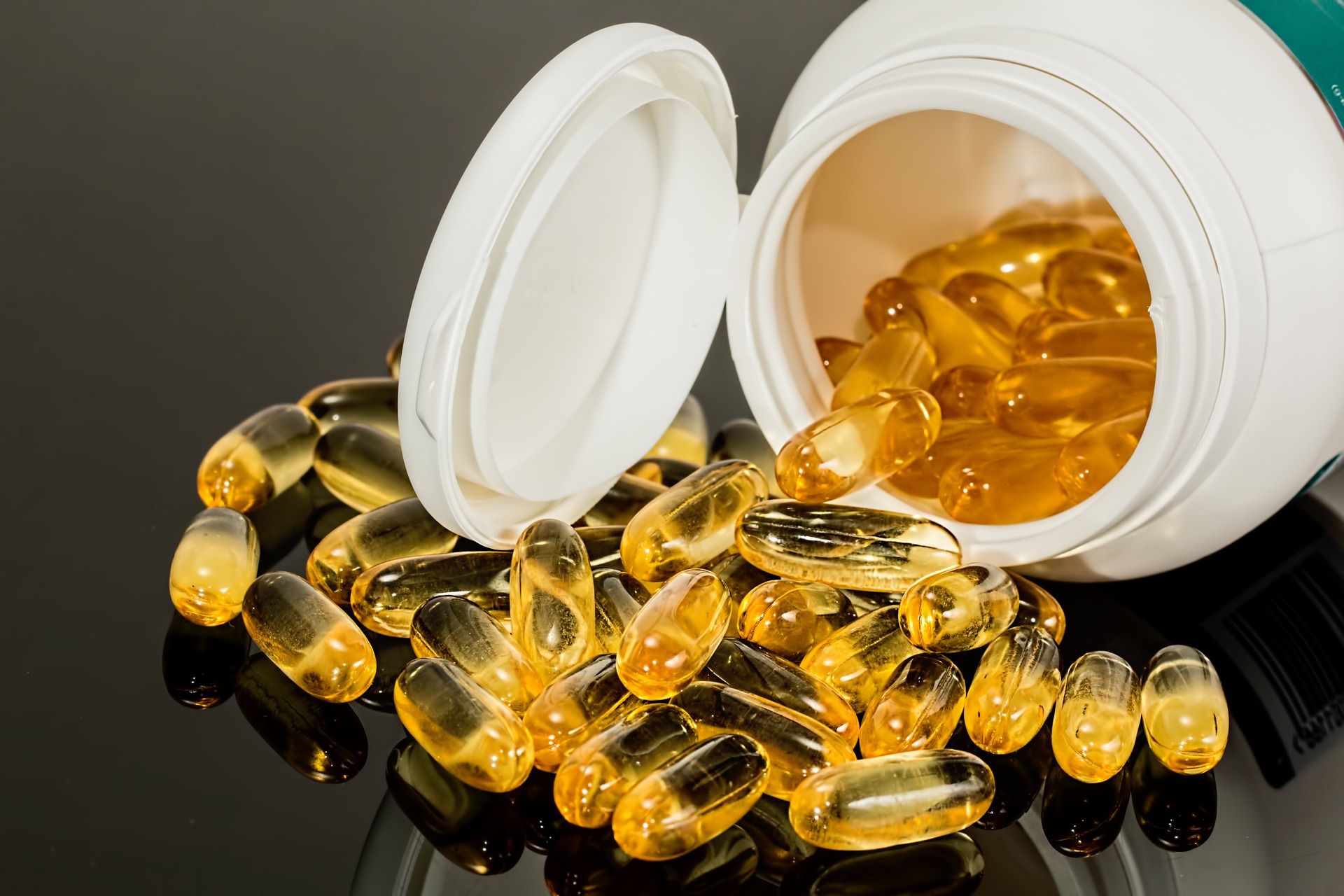 a white plastic bottle of transparent yellow pills spills onto a black countertop