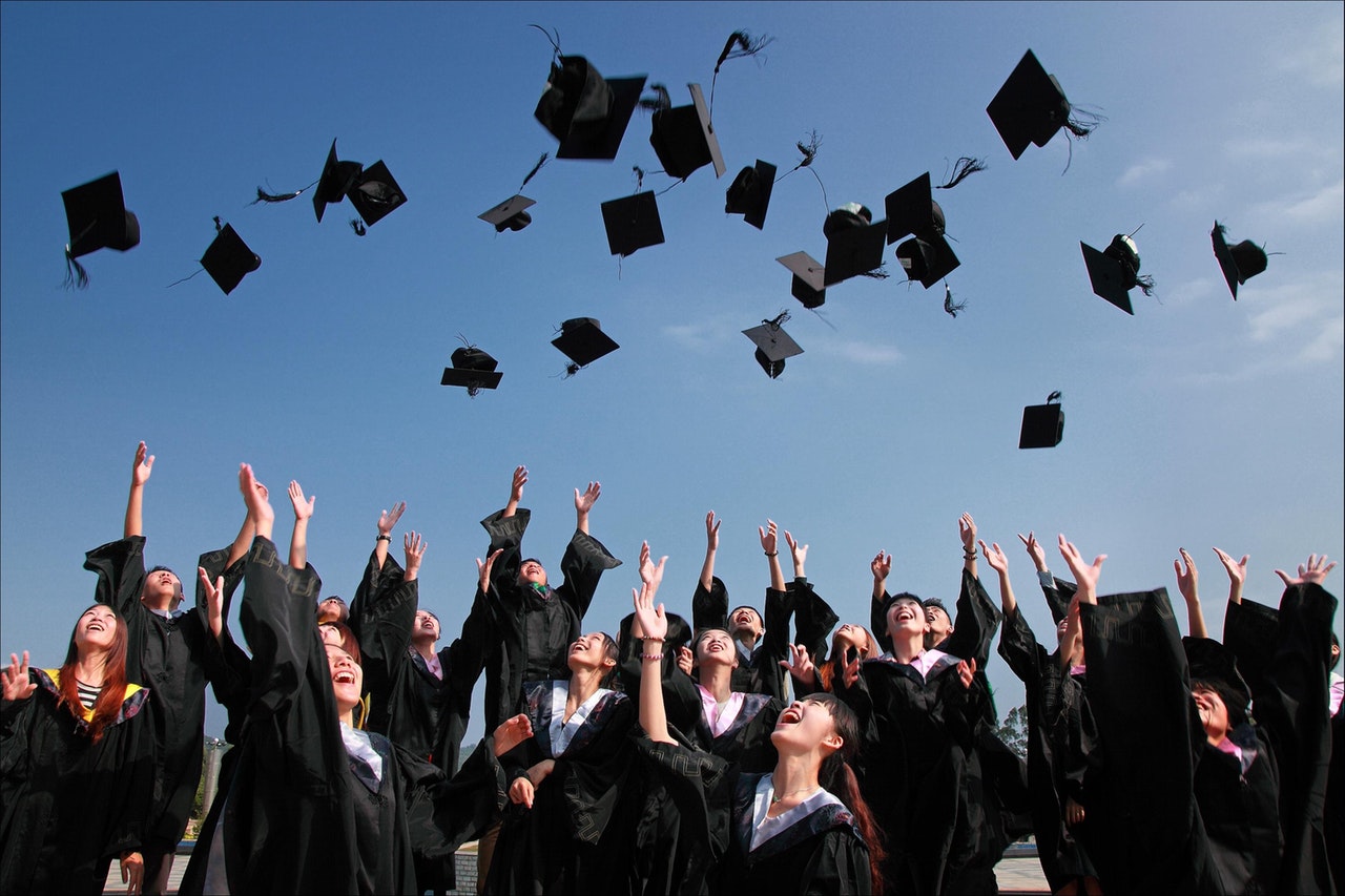 Graduates throw their graduation caps in the air against a bright blue sky.