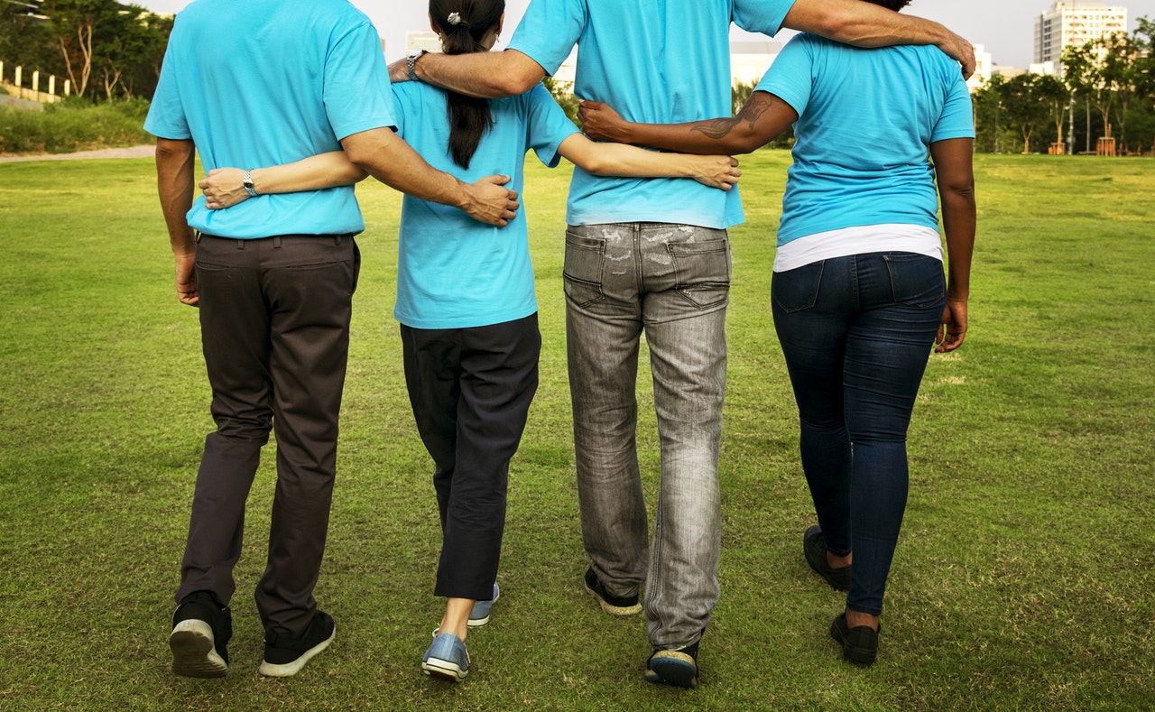 Four people wearing the same bright blue t-shirt walk away from the camera with their arms around each other's shoulders 