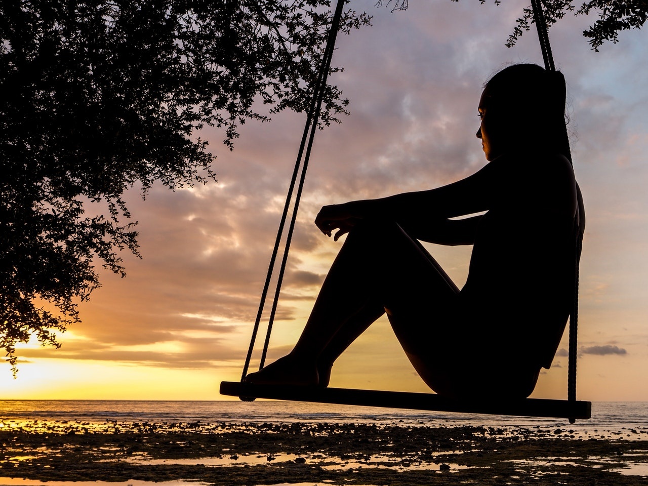 A woman sits on a swing watching a sunset