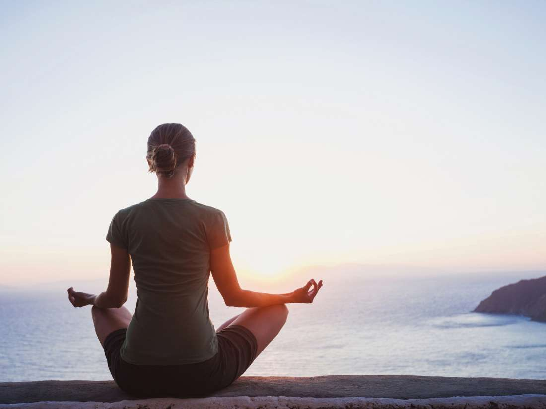 woman sitting and meditating in front of a huge body of water