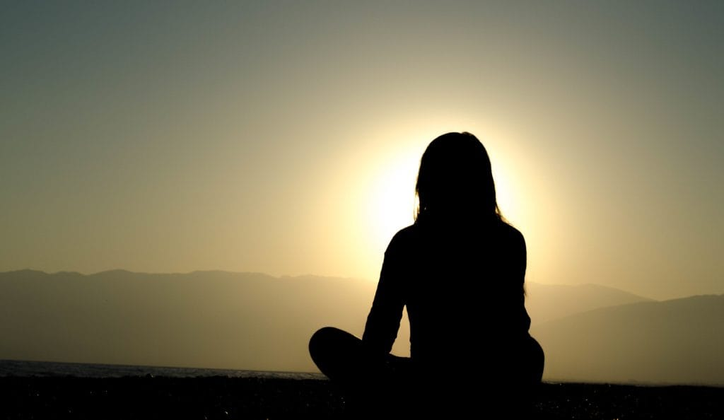 woman sitting and meditating in front of a sunset