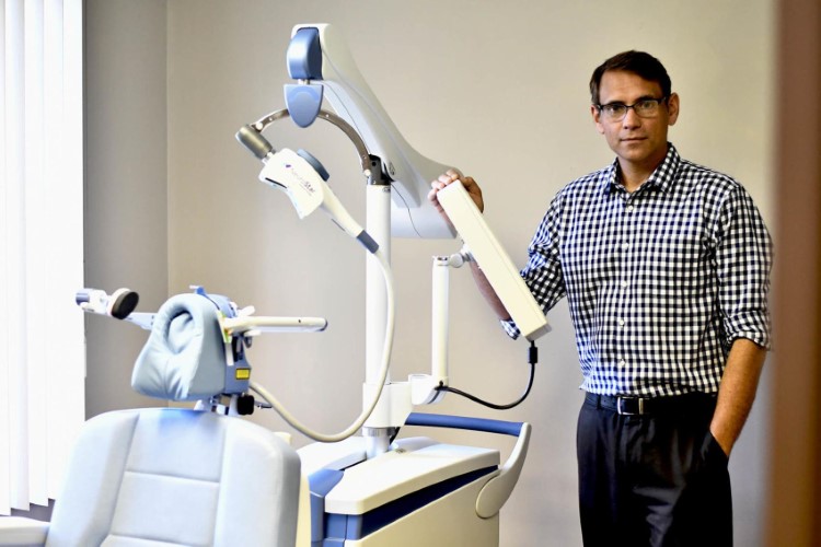 Male technician stands next to a transcranial magnetic stimulation (TMS) machine