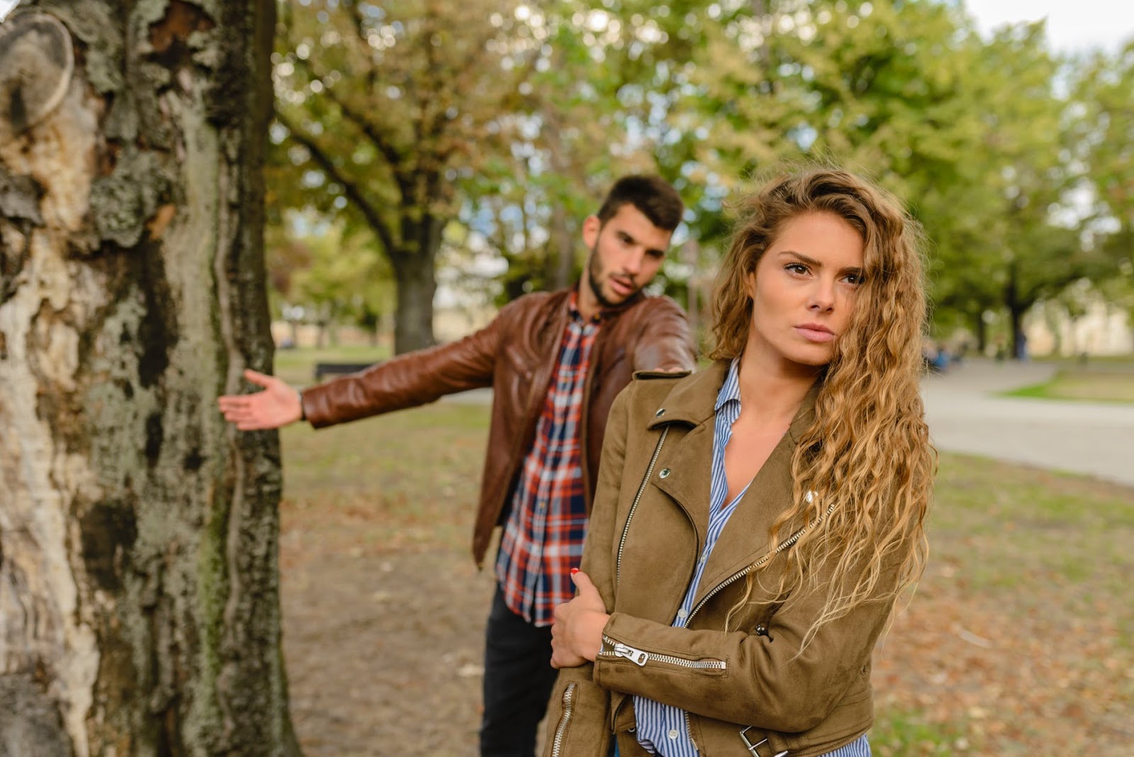 A man and a woman stand by a tree in the park while in a confrontation