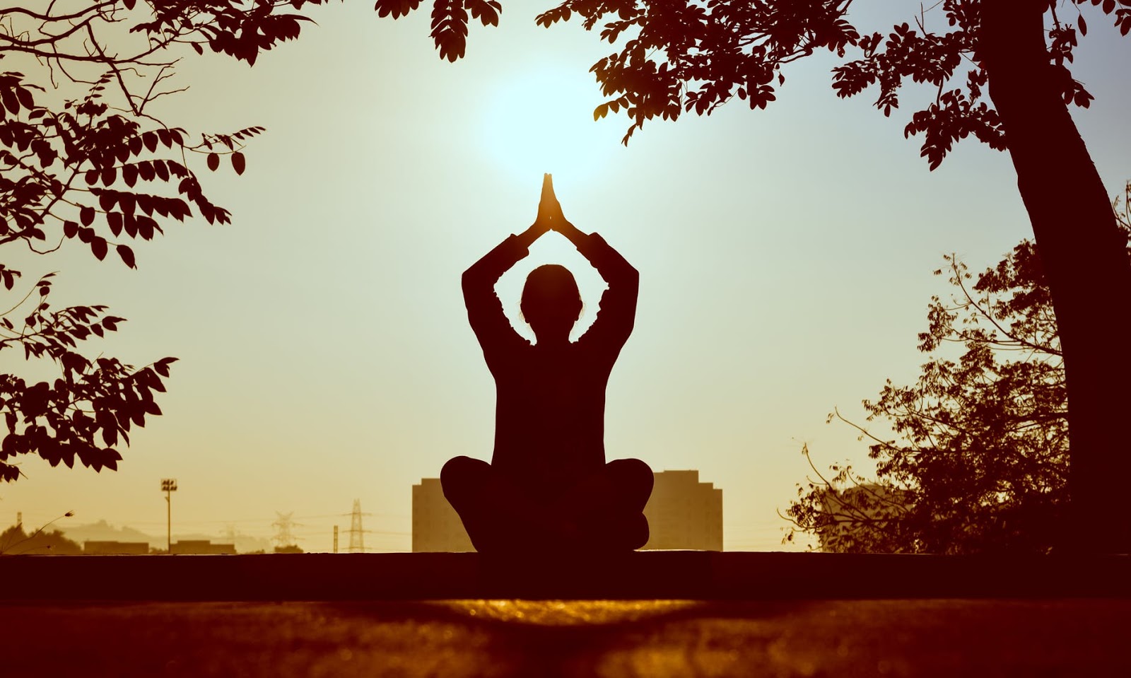 A woman sits in a meditative pose outdoors and facing towards the sun. 