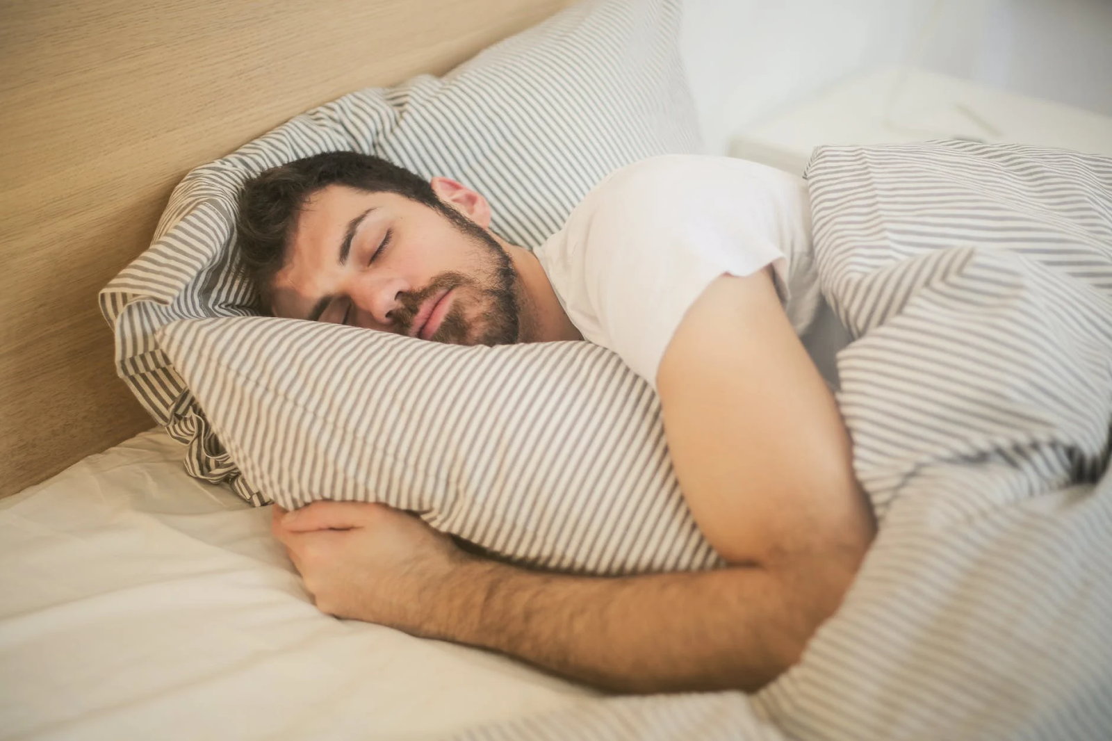 A man sleeps soundly in bed while hugging a pillow