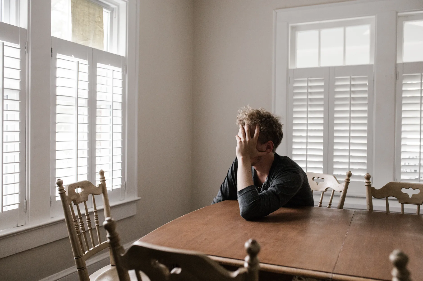 A man tiredly clutches his head in his hand as he leans across a dining room table