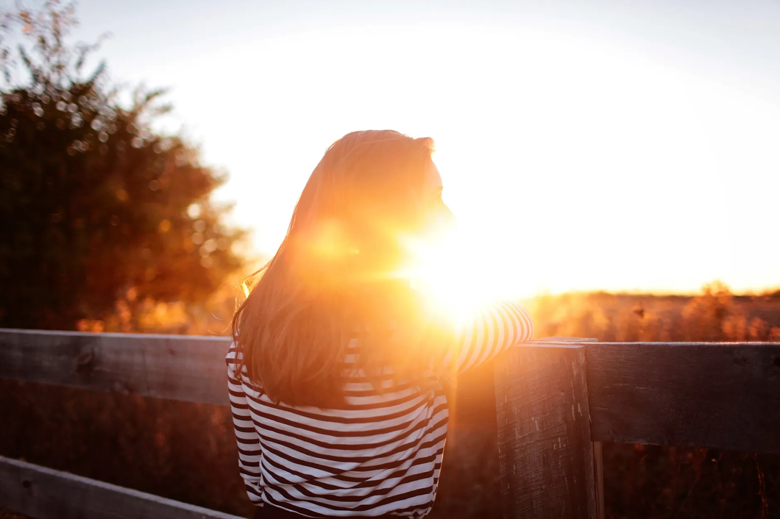 A woman stands outside, enjoying the sunshine beaming down on her