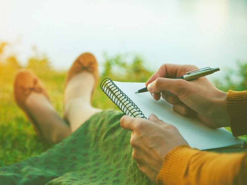 A woman sitting in grass penning something in her journal. 