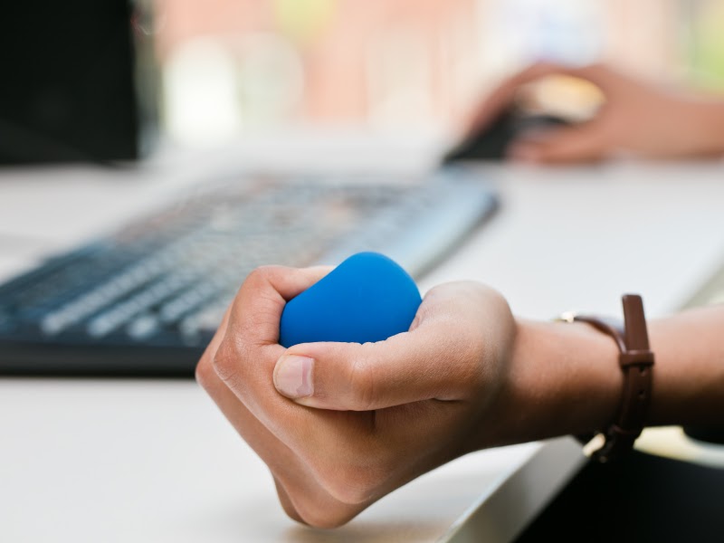 Someone at a desk firmly grasps a stress ball. 