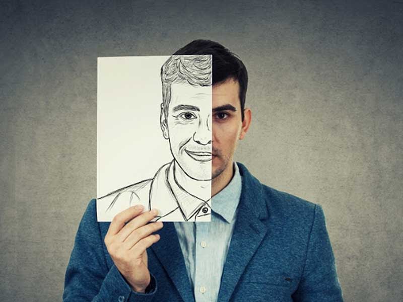 A sad looking man holds up a drawing of a happier self.
