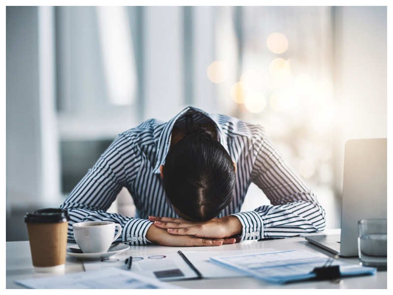 A frustrated woman sits with her head down at her desk.