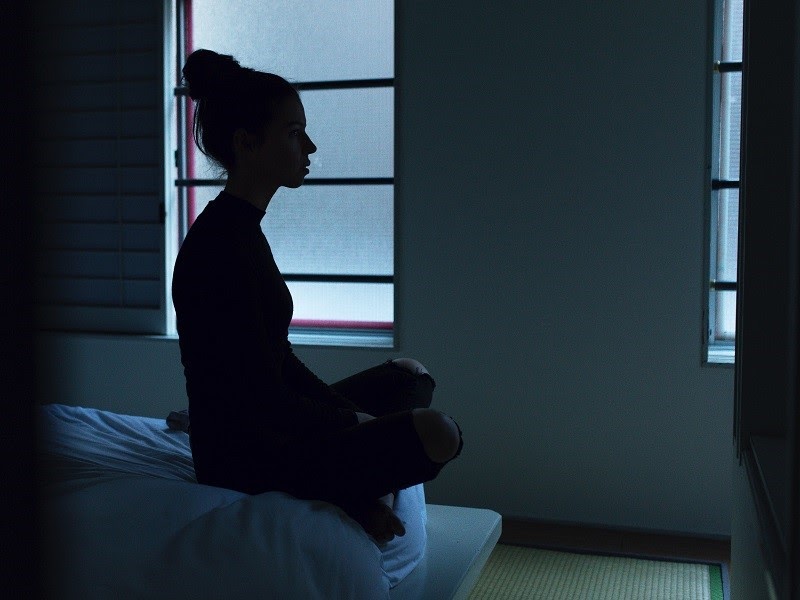 A woman sitting on her bed in a darkened room. 