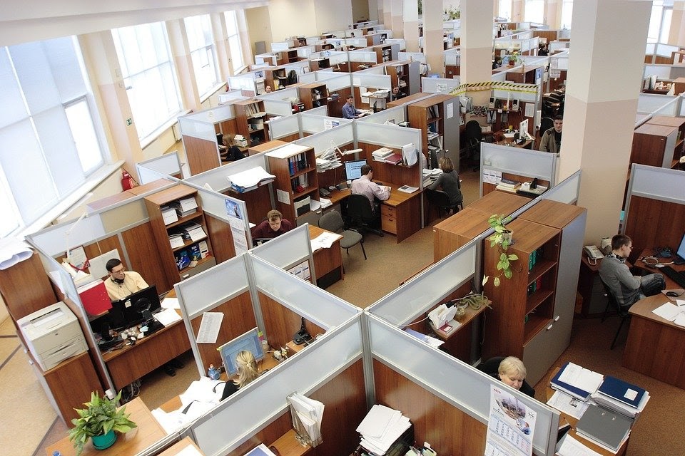 An image depicting an office space, full of cubicles and people at work.