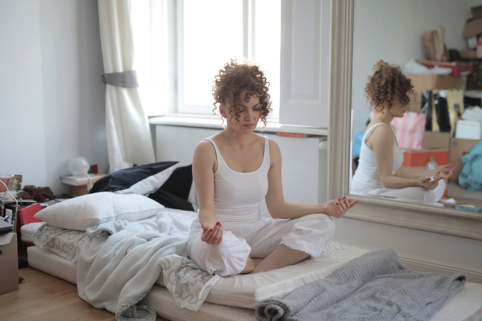 A woman meditating while sitting on a mattress on the floor 