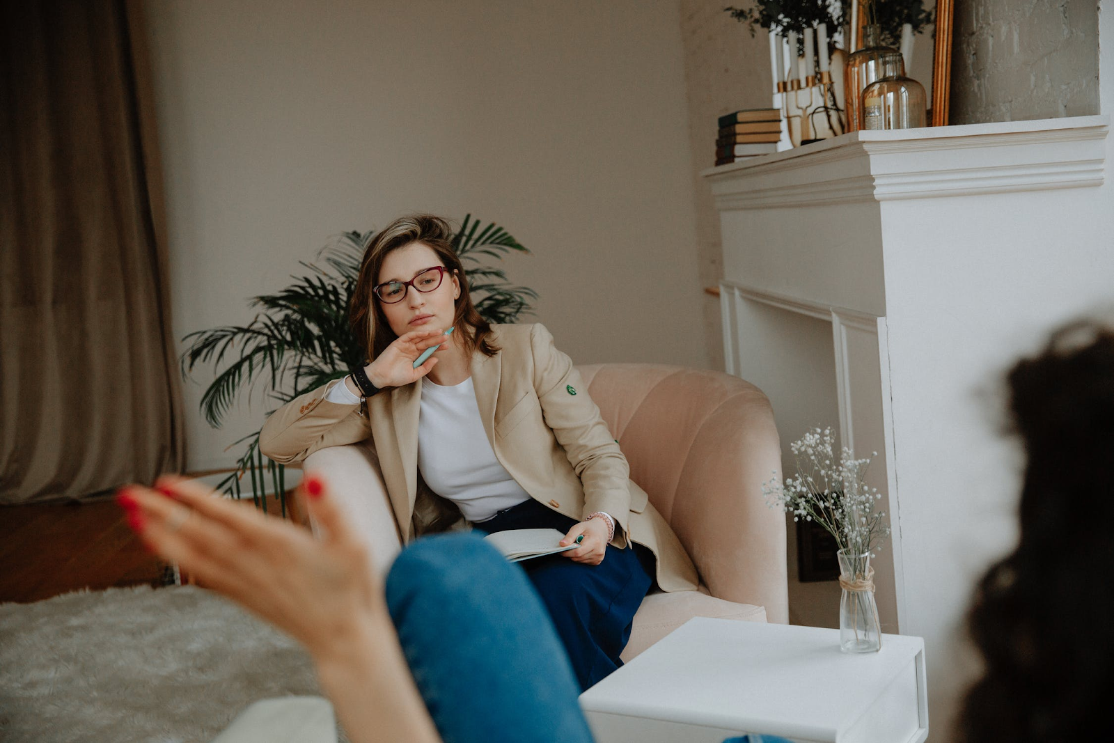 An image of a therapist sitting in a chair, listening and taking notes while her client speaks.