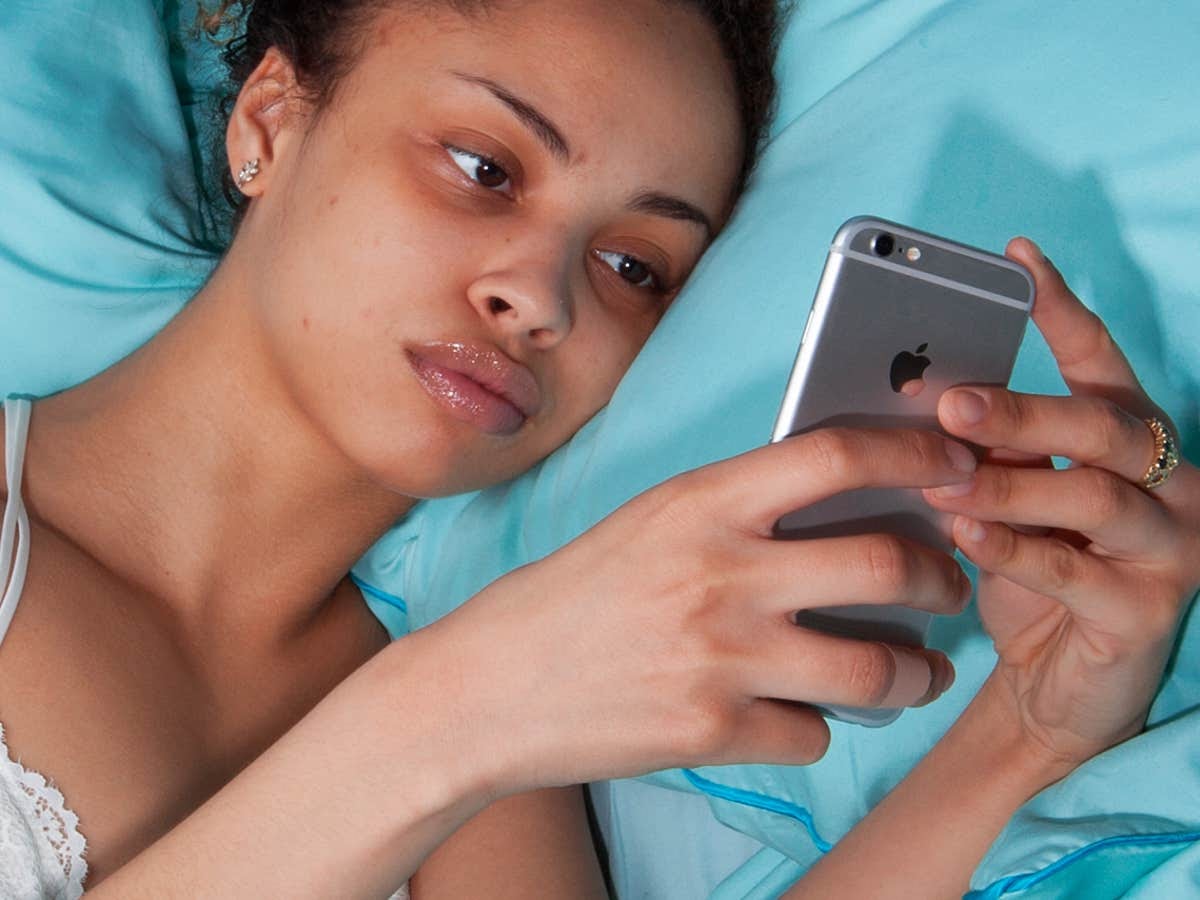 A woman lying down in bed and staring at her phone.