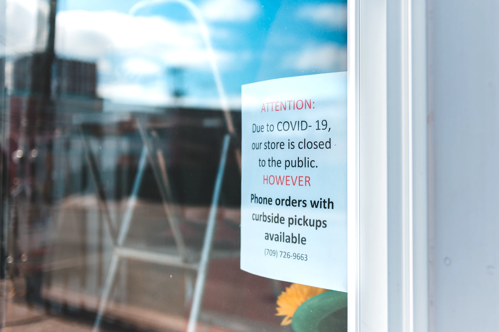 An image of a flyer in a store window that reads "Attention: due to COVID-19, our store is closed to the public. HOWEVER, phone orders with curbside pickups available."