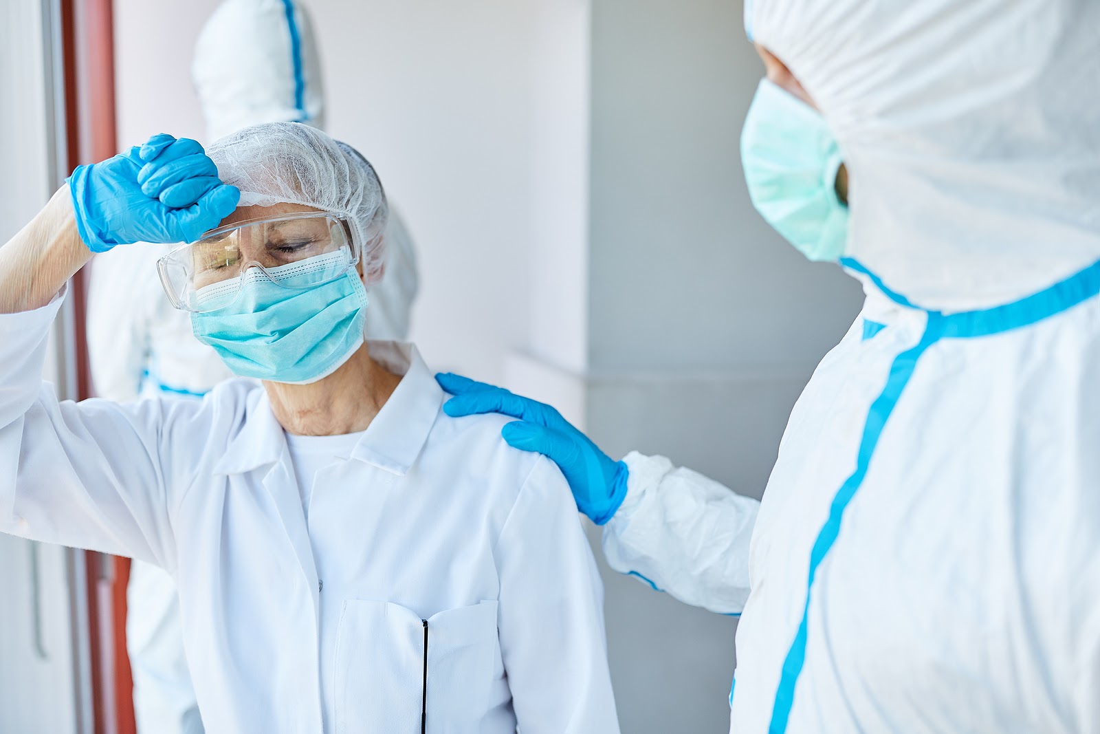 Two healthcare workers in PPE consoling each other.