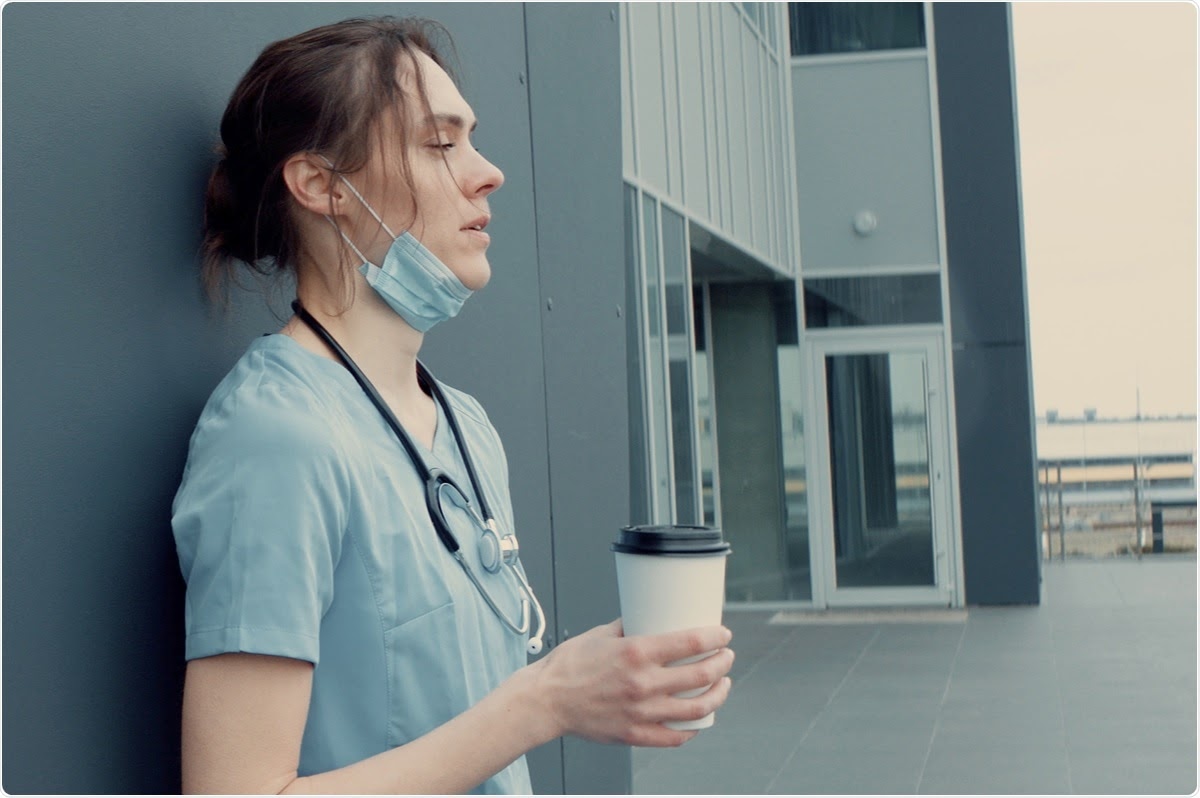 A healthcare worker standing outside of a building holding a cup of coffee.