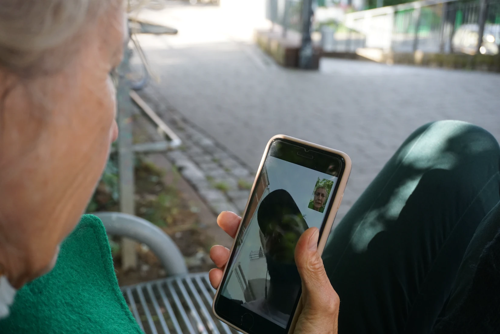 An image of an old woman holding a phone in her hand. She is on a video call with a man in a baseball cap.