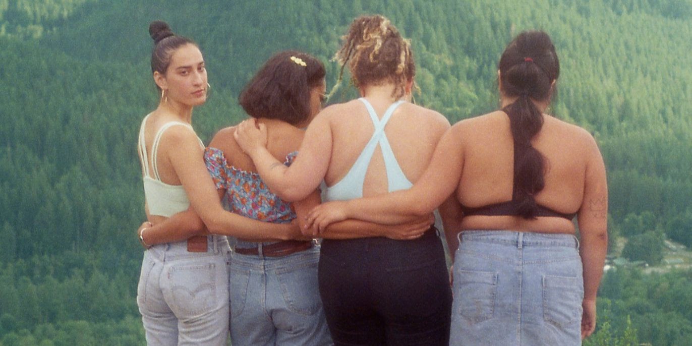 Four friends standing with their arms wrapped around each other. Three of them are looking at the mountains and one is looking behind them.