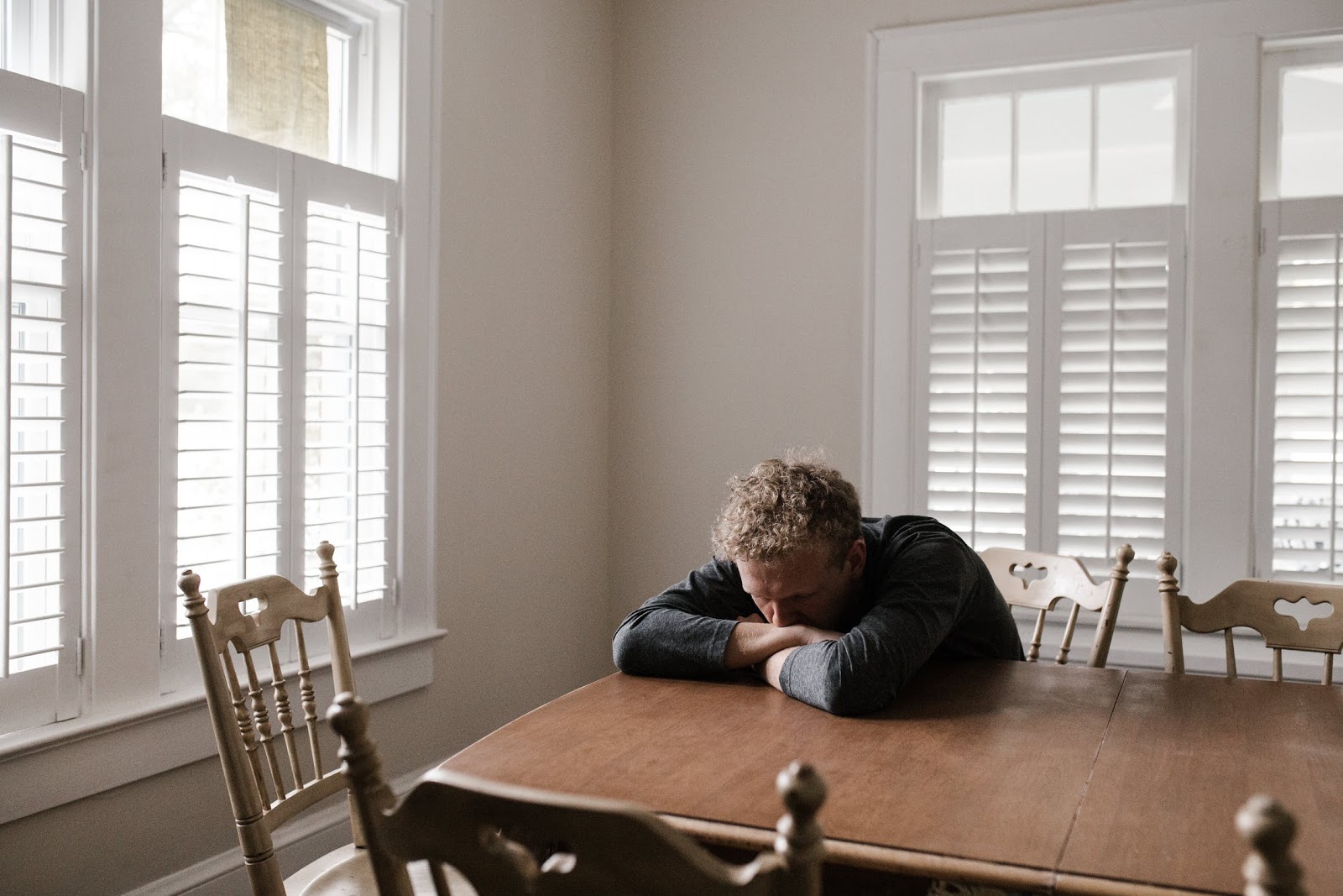 A disappointed man sitting at a dining room table with his head down.