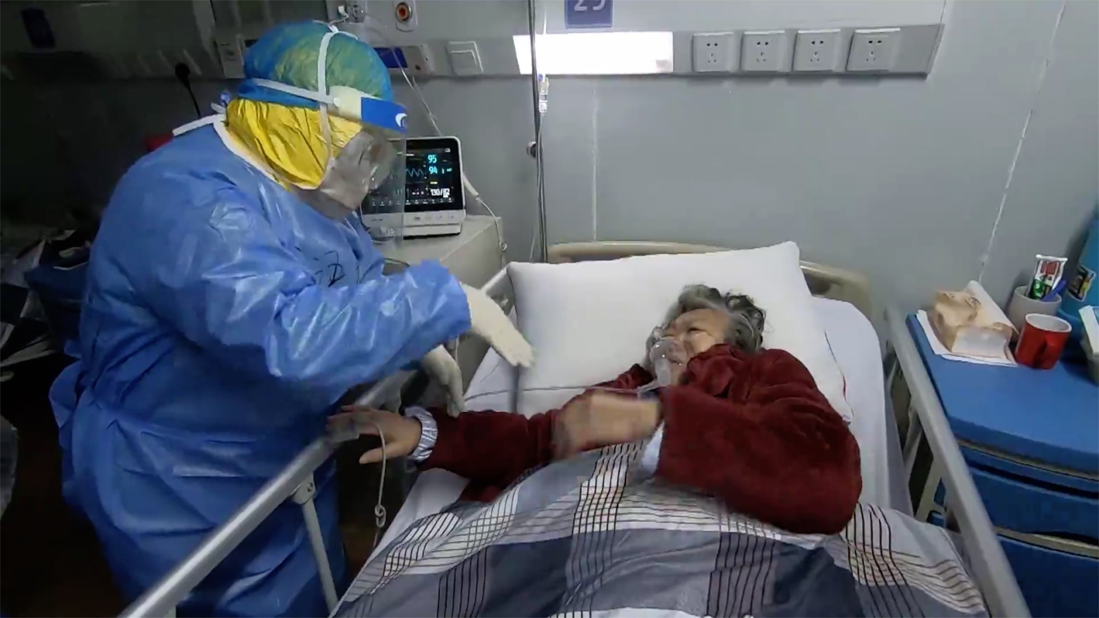 A health care worker wearing PPE gives aid to an elderly woman suffering from COVID-19.