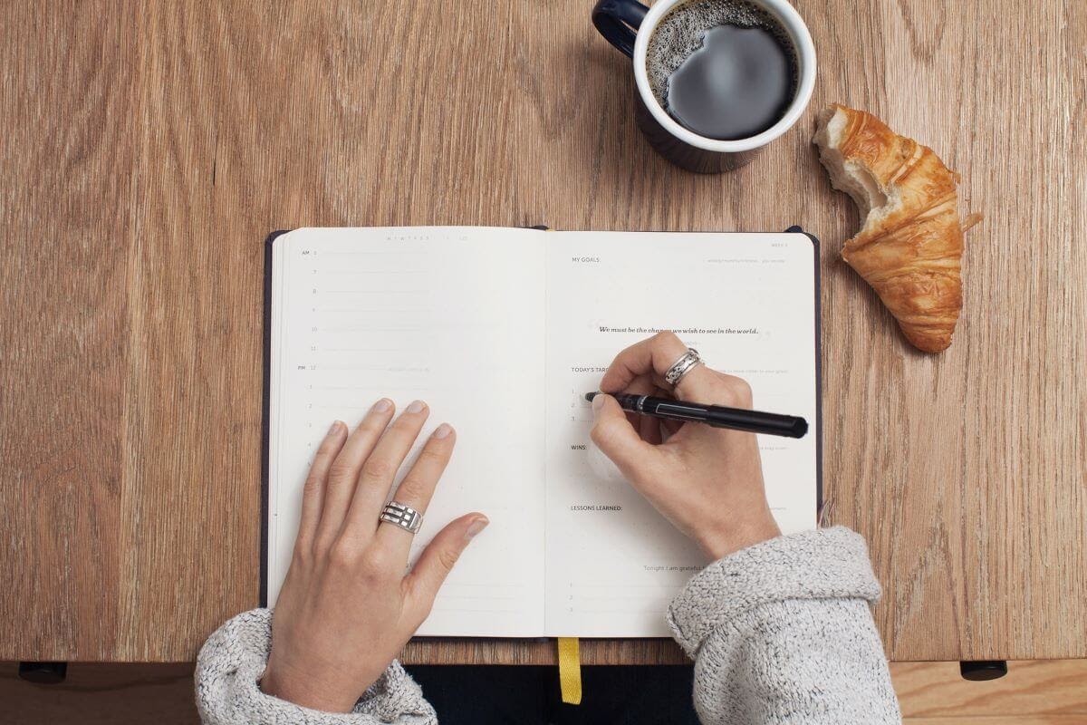 Woman Writing in a Planner With Coffee and a Croissant