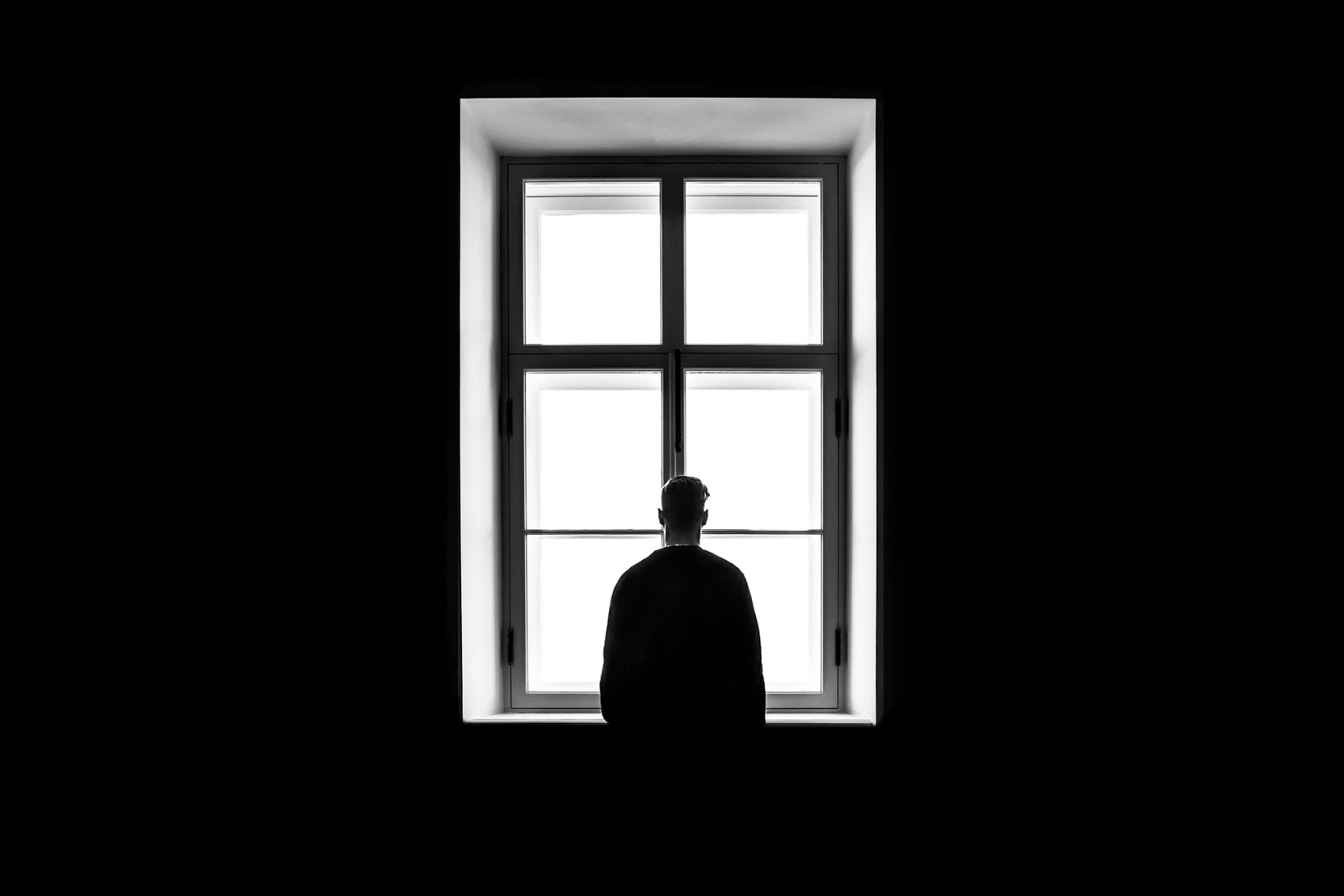 A man looking out a window symbolizing being alone.