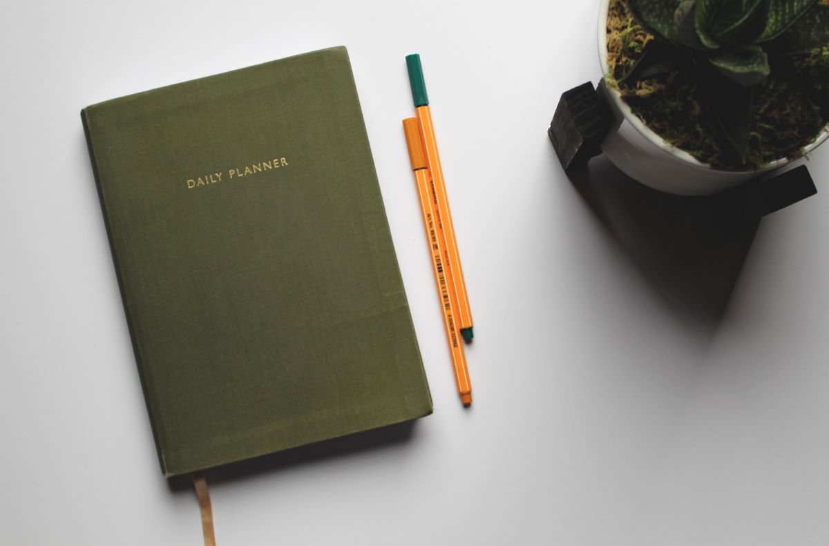 A Tidy Daily Planner with Pencils Next to a Plant